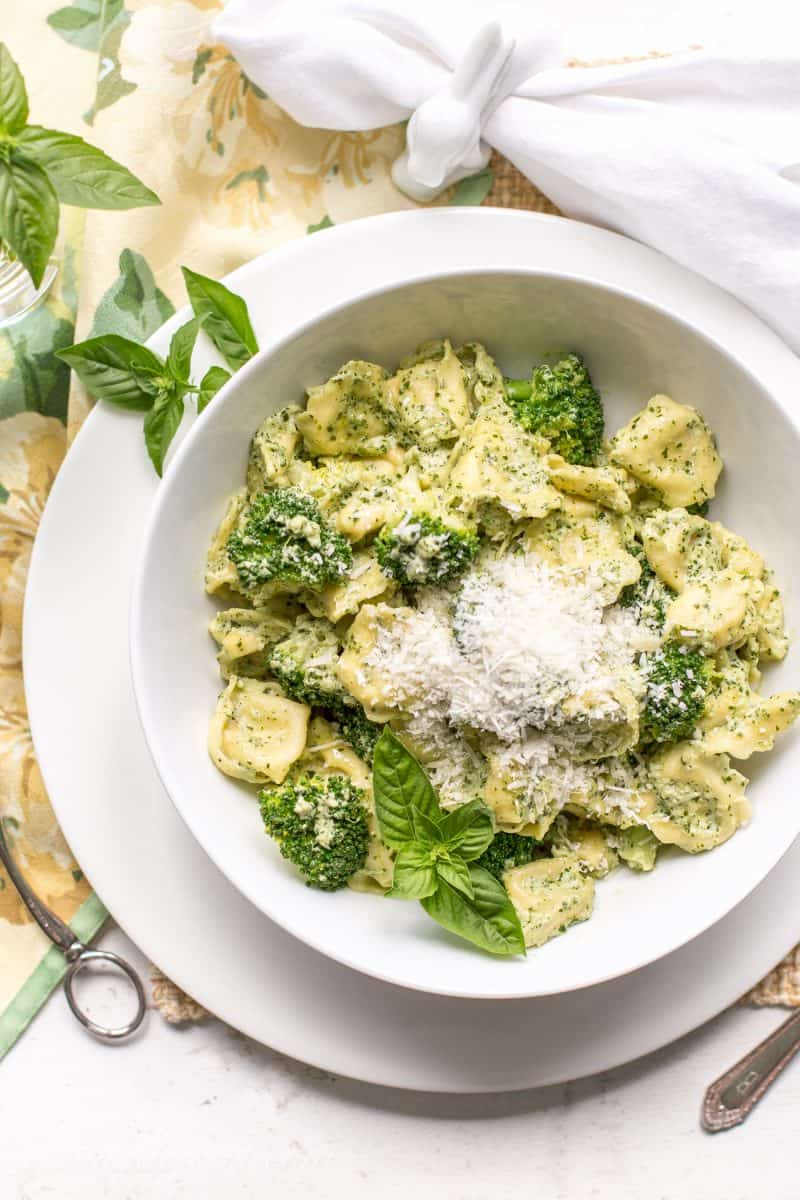 A bowl of tortellini pasta with broccoli, fresh basil and a pesto cream sauce