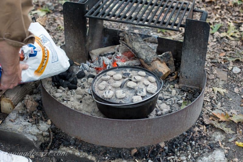 A campfire ring with a Dutch oven covered in hot coals