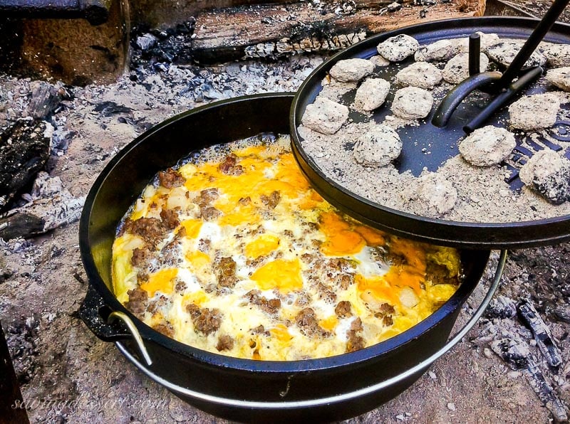 A Dutch Oven set over an open fire filled with a sausage and hash brown breakfast casserole