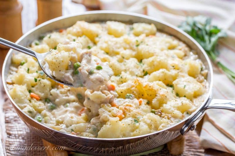 A large skillet with creamy chicken and vegetables topped with buttery, browned potato chunks
