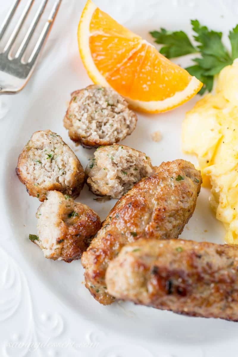 An overhead view of several links of homemade sausage on a plate with eggs and an orange slice