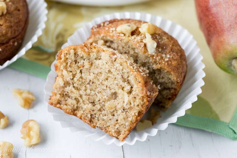 A muffin broken open showing a moist tender interior. Topped with walnuts and filled with chunks of pear