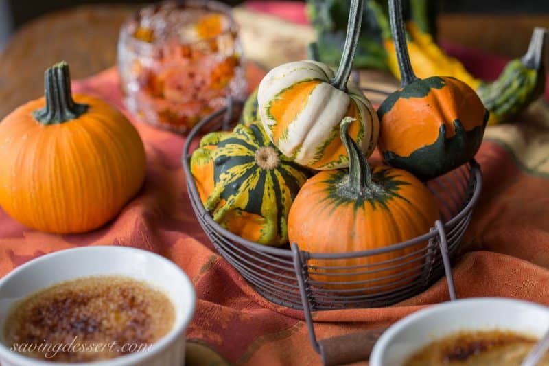 Mini pumpkins and gourds in a basket on a table with pumpkin creme brûlée