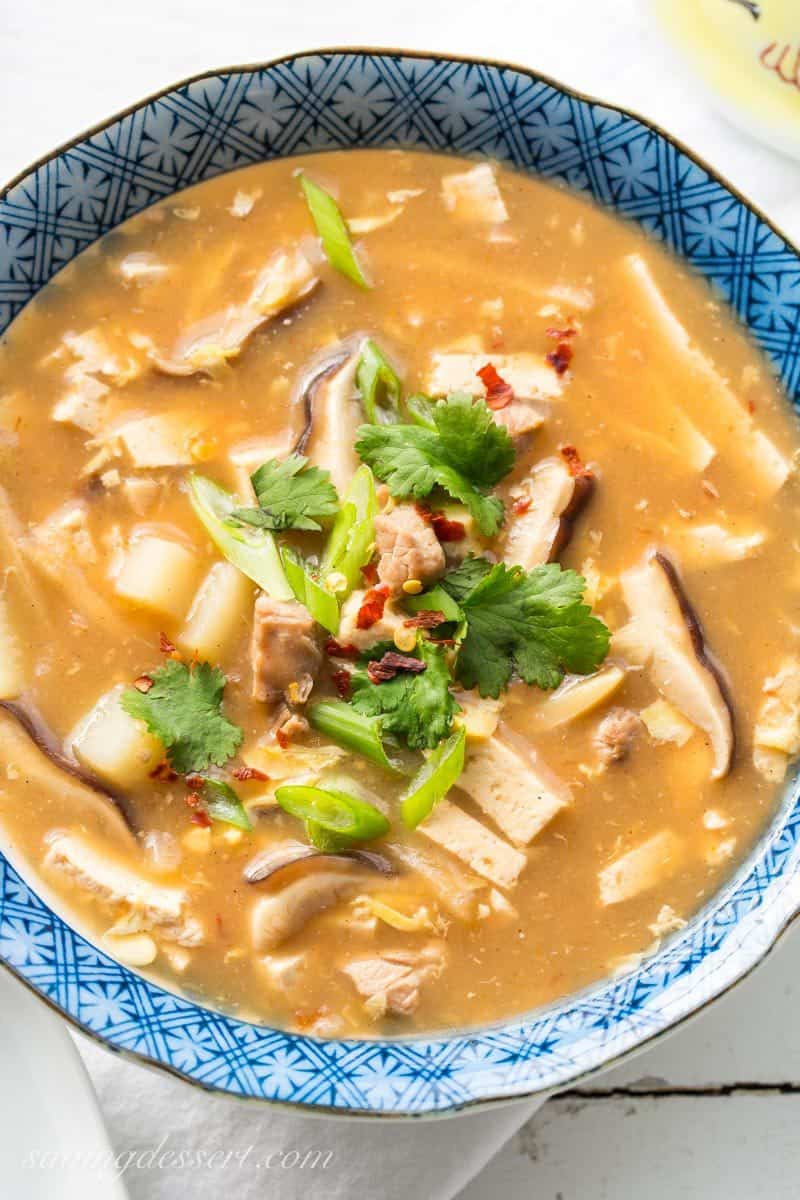 A bowl of hot and sour soup garnished with cilantro and loaded with mushrooms and tofu