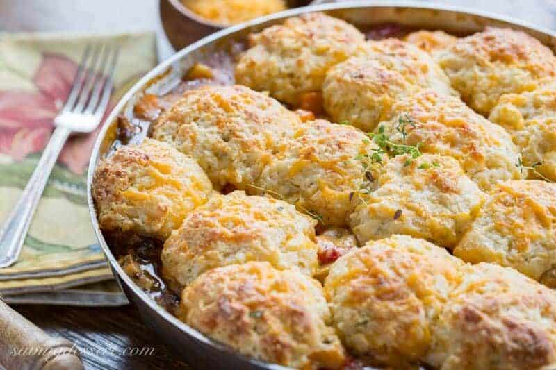 A bubbling skillet filled with vegetables topped with golden brown herb and cheese biscuits