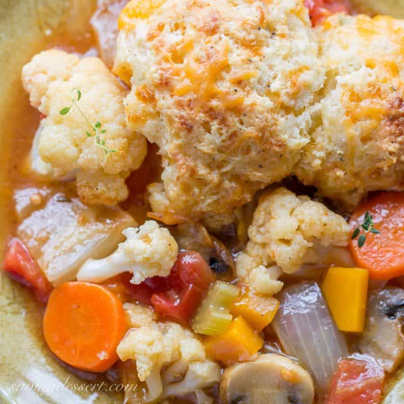 Savory winter vegetable cobbler in a bowl with cheesy herbed biscuits on top