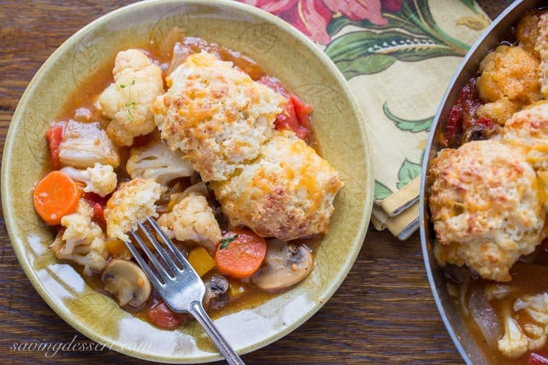 A bowl with vegetables in a rich broth topped with cheesy herb biscuits in a savory winter vegetable cobbler