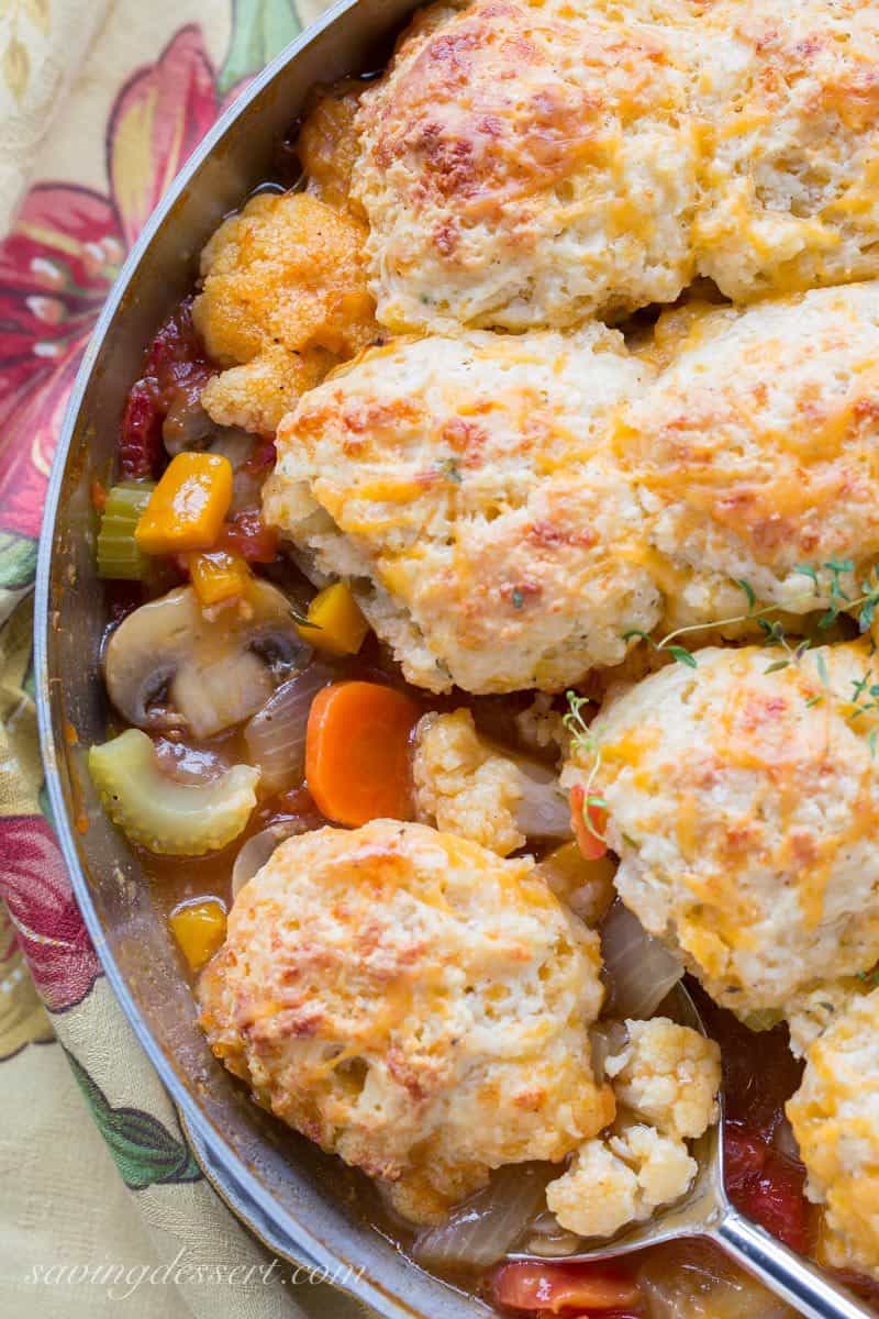 An overhead view of a skillet filled with mushrooms, celery and carrots topped with cheesy biscuits