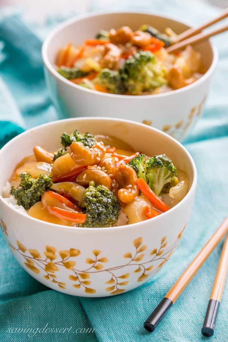 Two bowls of rice topped with stir fried vegetables in a sticky sauce