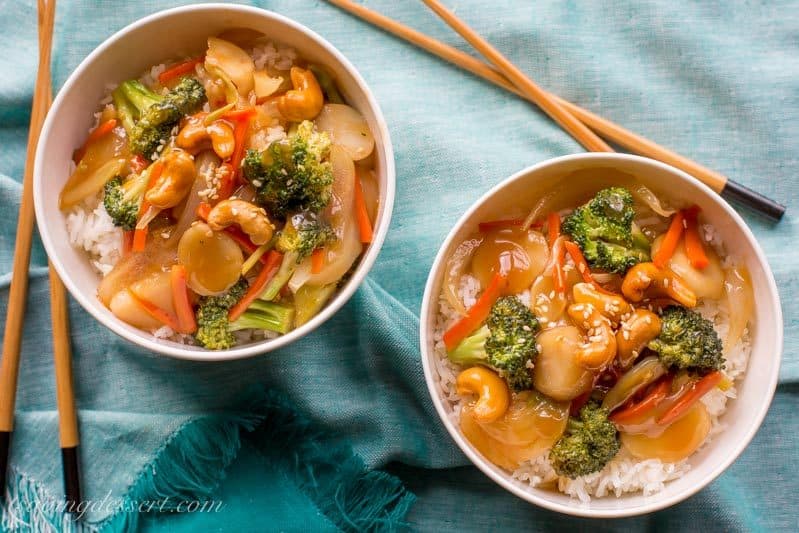 Overhead view of two bowls of stir fry vegetables served over rice with chop sticks