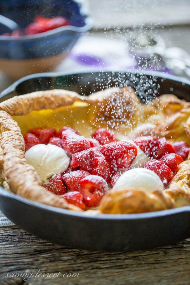 A Dutch Baby in a cast iron skillet being topped with powdered sugar