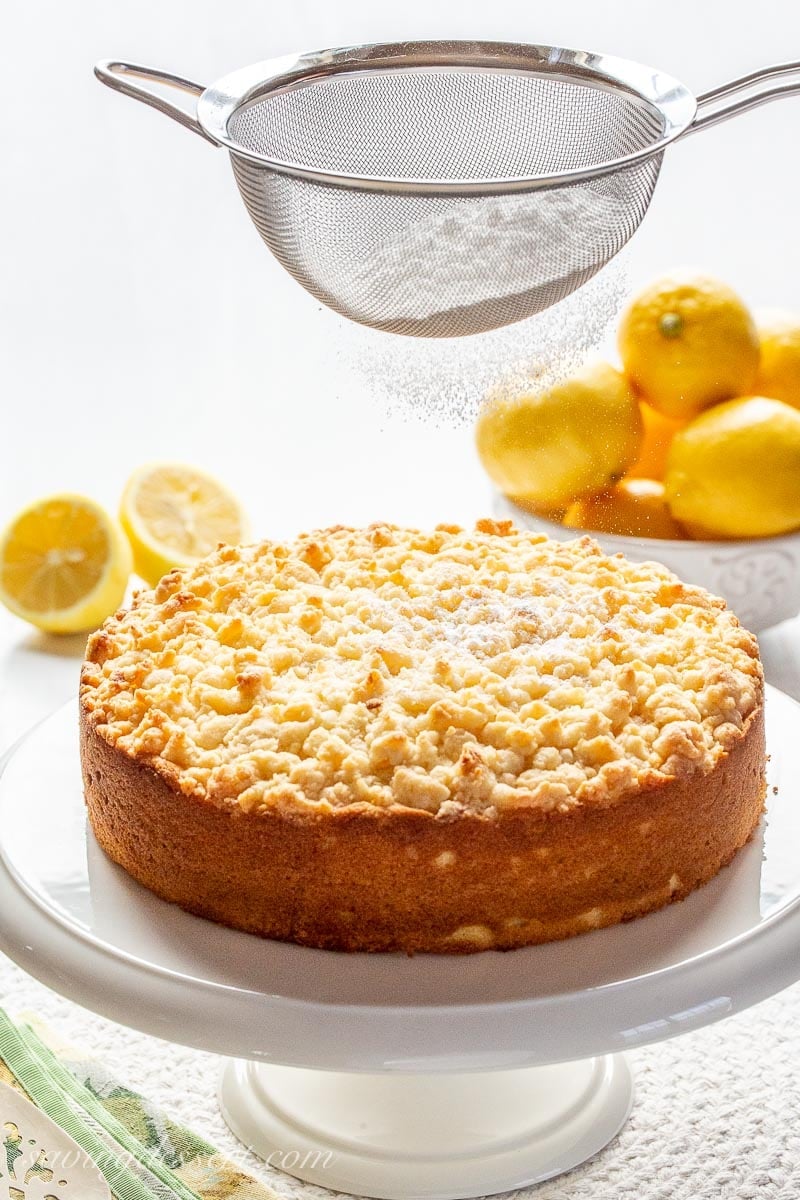 A single layer cake on a cake stand being dusted with powdered sugar