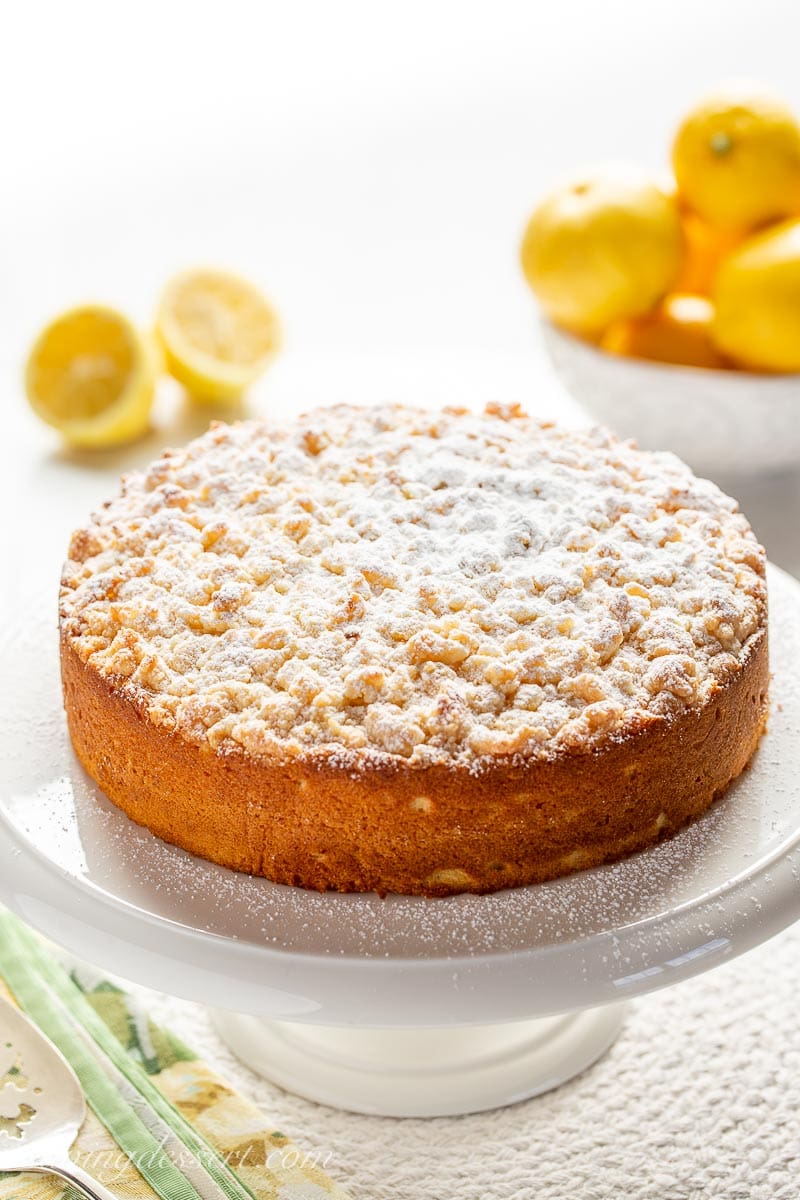 Lemon Crumble Breakfast Cake on a cake stand with lemons