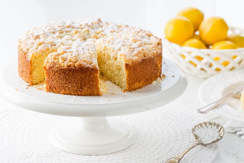 A lemon crumble cake sprinkled with powdered sugar on a cake stand 