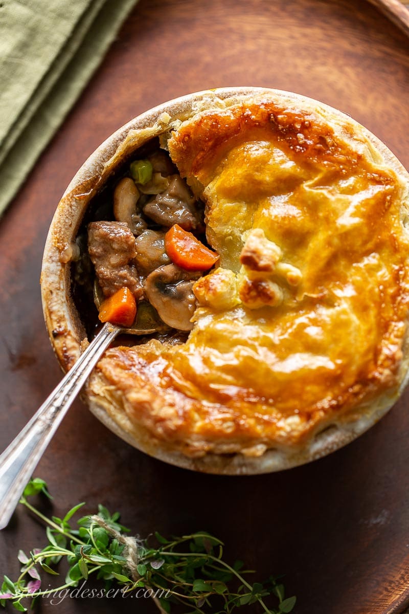 A beef pie with carrots and peas topped with golden brown puff pastry