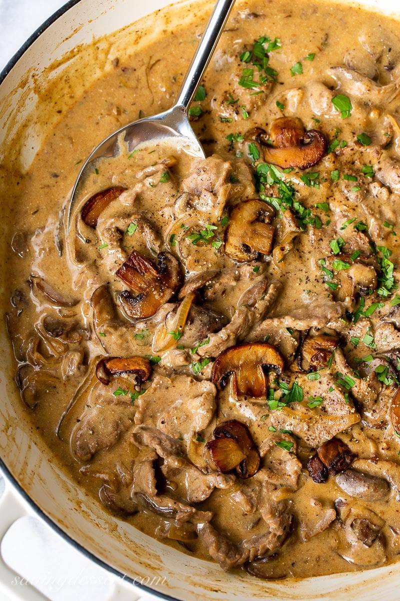 A skillet filled with mushrooms, gravy and sliced beef garnished with parsley