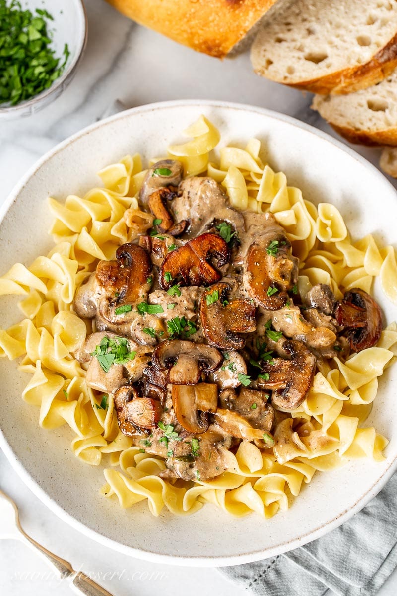 A bowl of egg noodles topped with Beef Stroganoff garnished with parsley