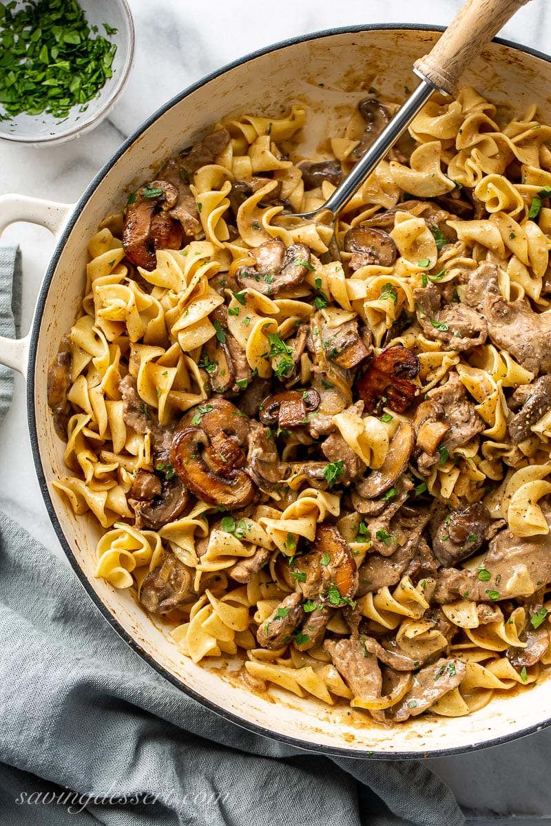 A skillet filled with beef, noodles and mushrooms in a creamy sauce