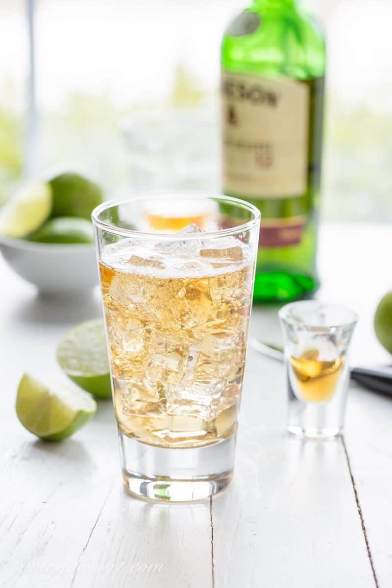 A tall glass of jameson and ginger ale with ice and lime wedges