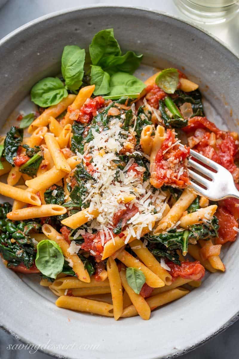 A bowl of kale, tomatoes and pasta with fresh grated Parmesan and basil leaves