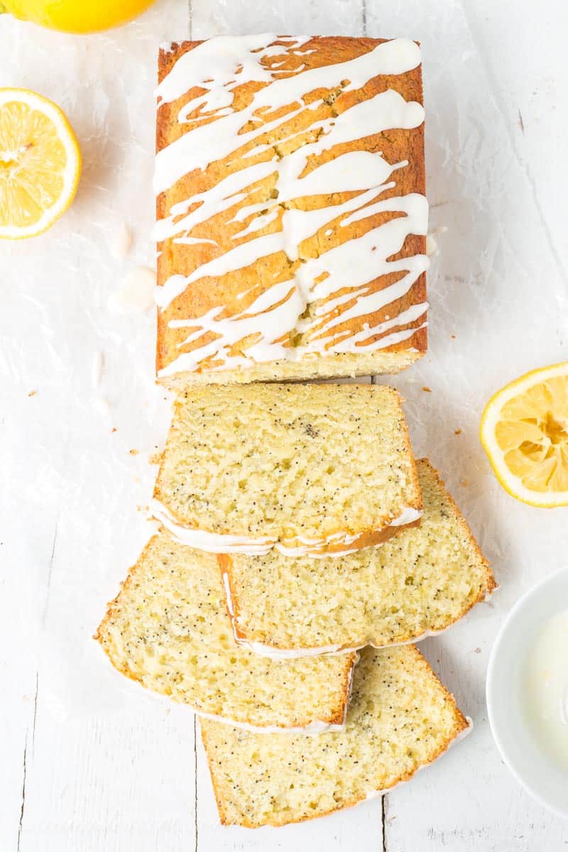 An overhead view of a loaf of lemon poppy seed bread, sliced and topped with a drizzle of lemon icing