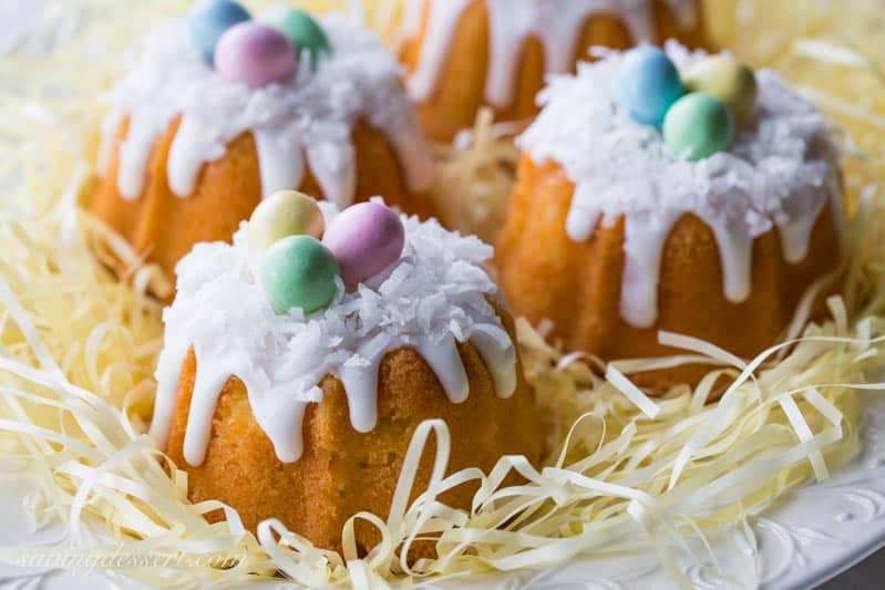 Mini Coconut Pound Cakes all dressed up for Easter fun! Baked in a mini bundt pan, topped with a simple coconut flavored icing and garnished with shredded coconut and pastel colored candy eggs. www.savingdessert.com