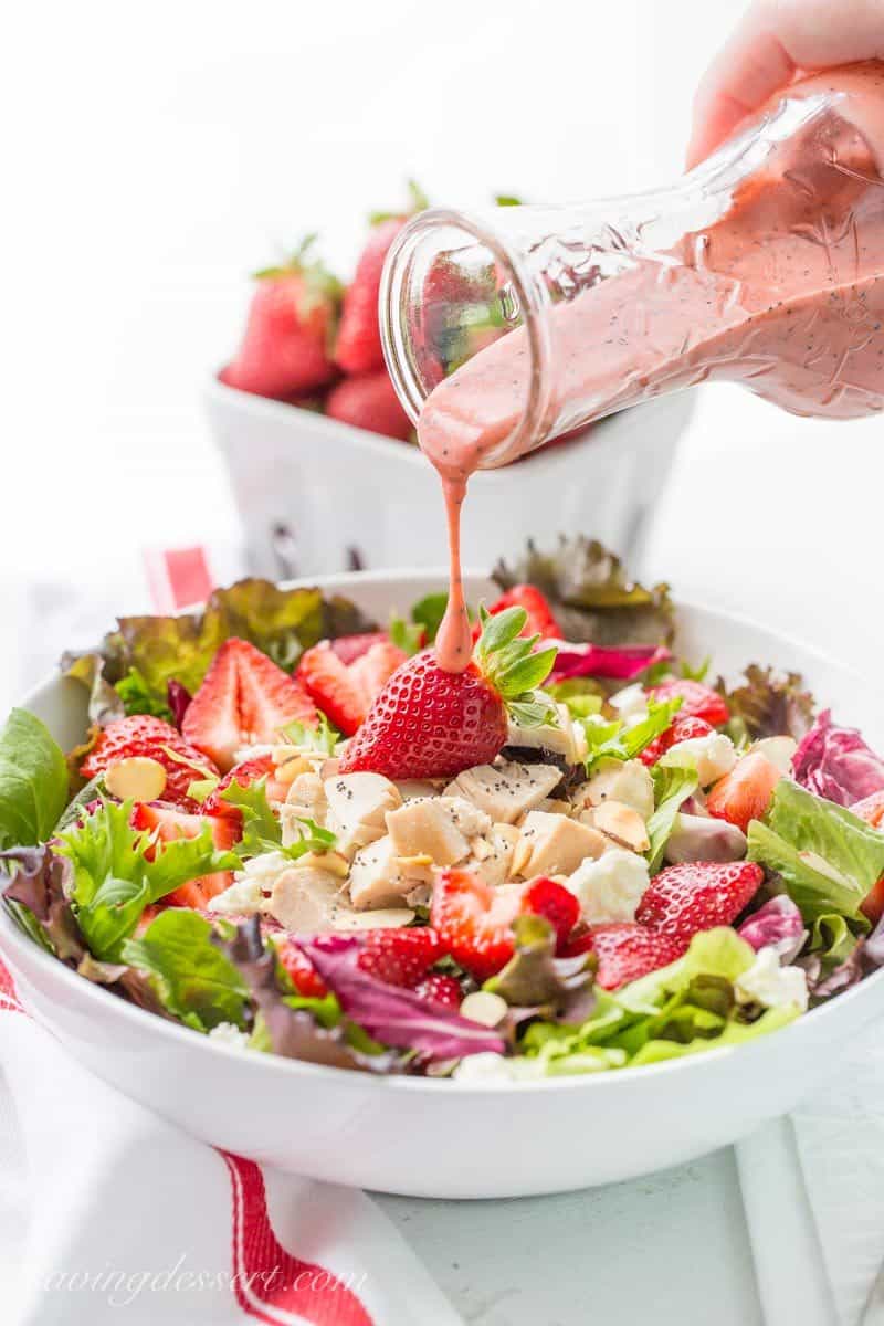 A bowl of salad with fresh strawberries and chicken drizzled with a poppy seed strawberry dressing