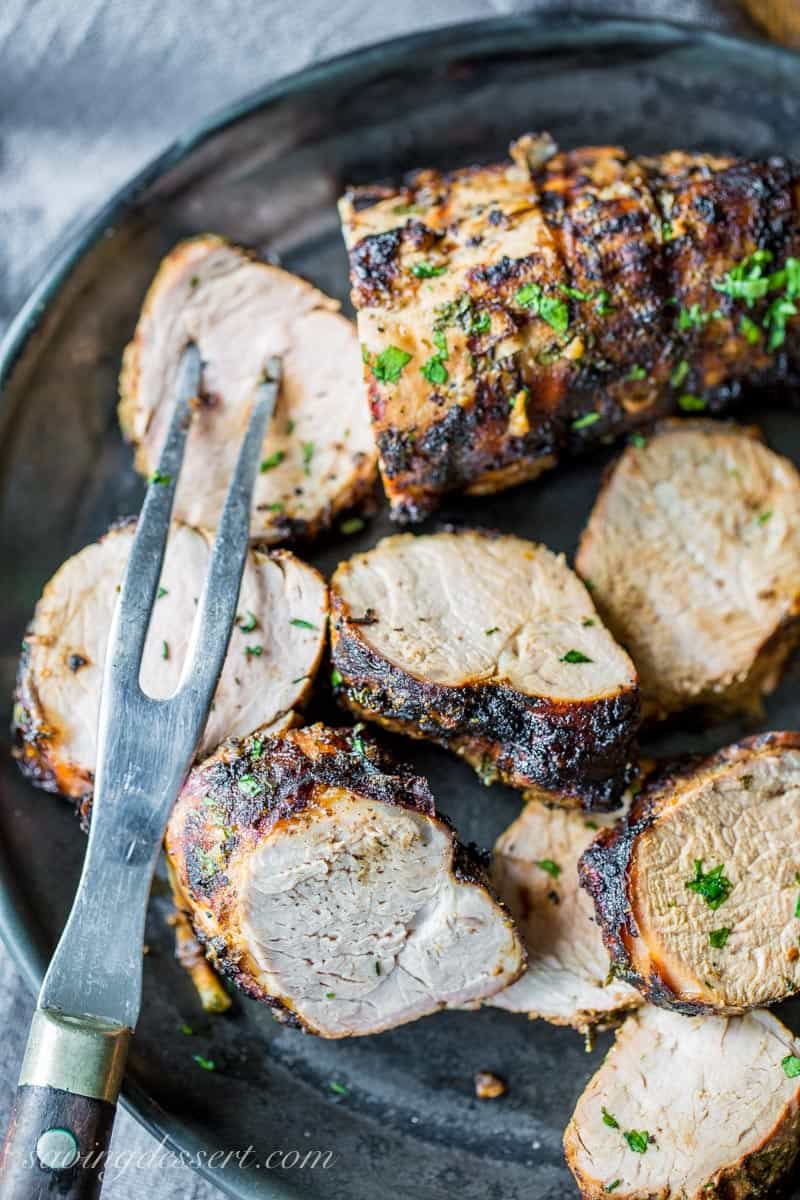 A grilled, sliced pork tenderloin on a black plate