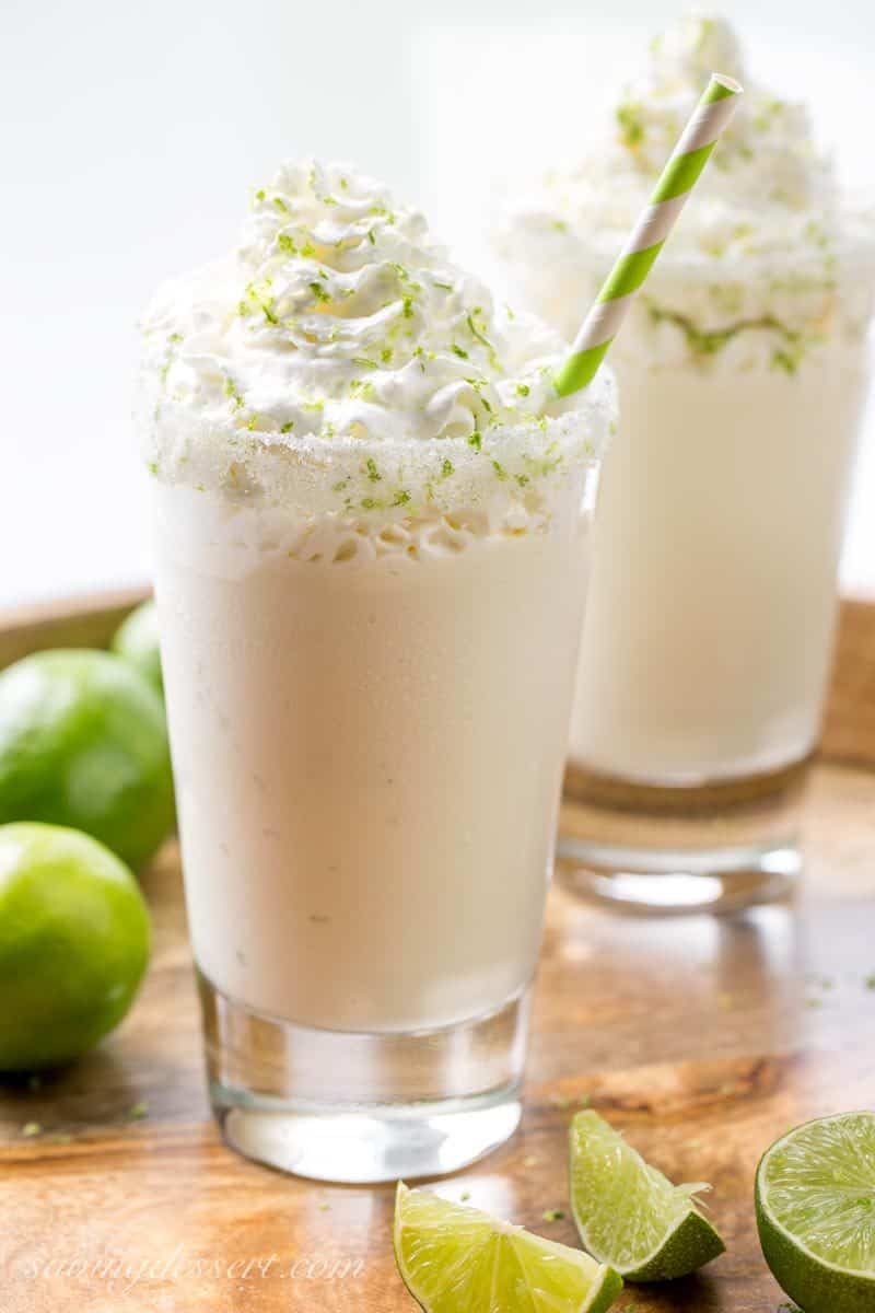 Two glasses filled with a milkshake with whipped cream and lime zest