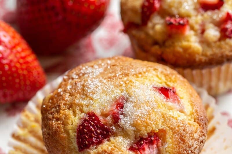 A closeup of a strawberry muffin on a plate with fresh strawberries on the side
