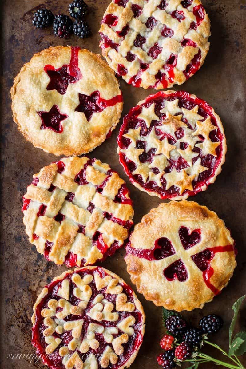 Six blackberry tarts with various designs on top with golden brown crust