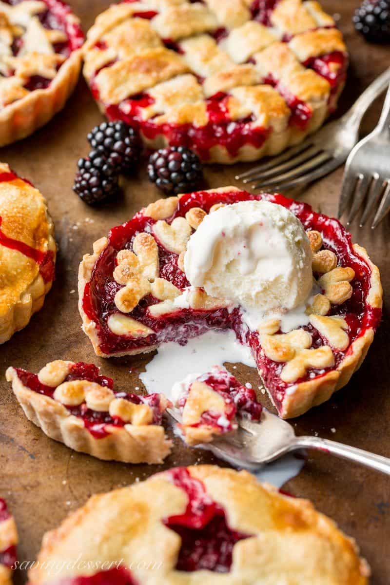 Mini Blackberry Tarts on a baking pan topped with with vanilla ice cream