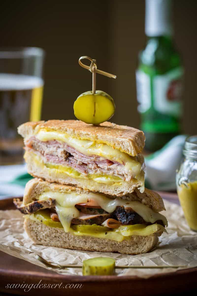 A stacked cuban sandwich with a pickle on top showing melted cheese in the middle