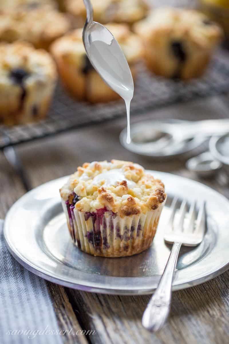 A lemon blueberry muffin with a crumble top drizzled with a lemon icing