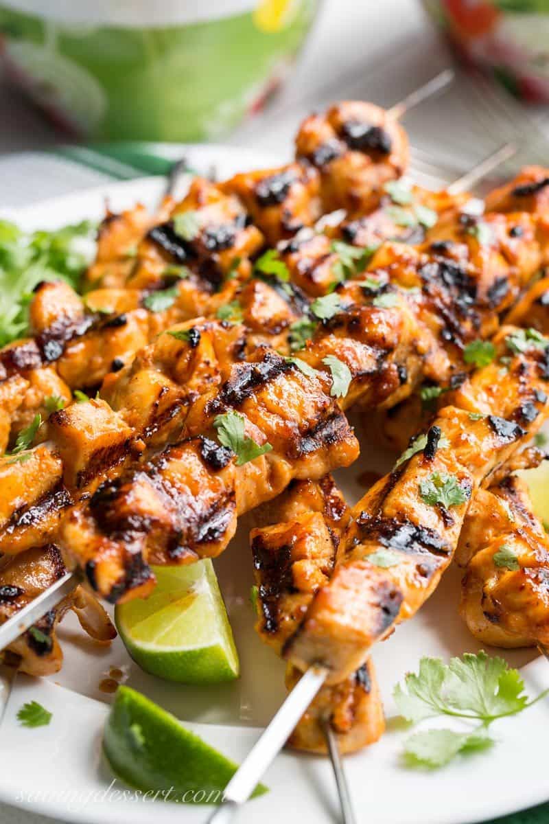 Chicken skewers on a plate garnished with cilantro and limes