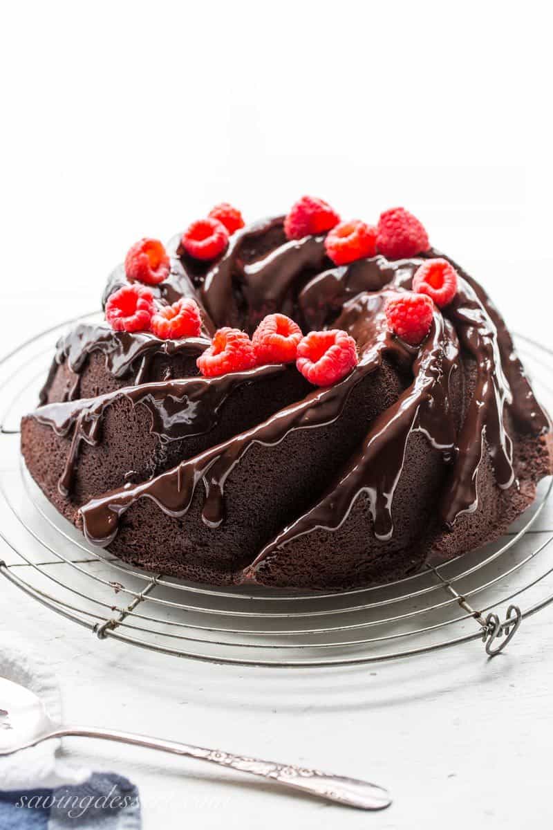 A chocolate bundt cake topped with raspberries on a wire rack