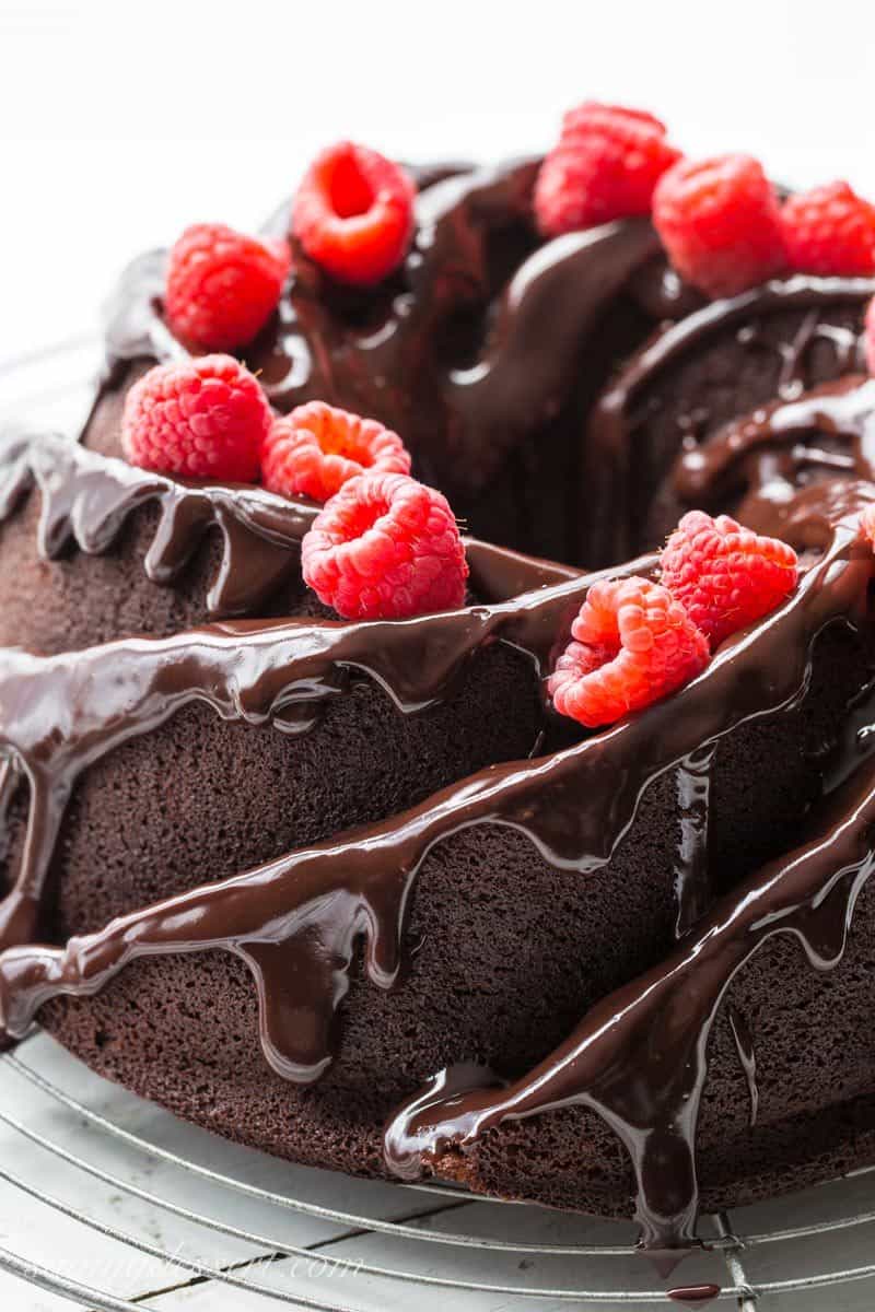 A closeup view of a chocolate bundt cake topped with drizzled chocolate and raspberries