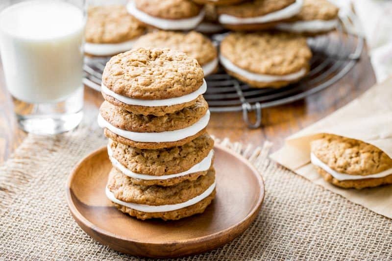 Oatmeal Cream Pies stacked on a wooden plate with a glass of milk