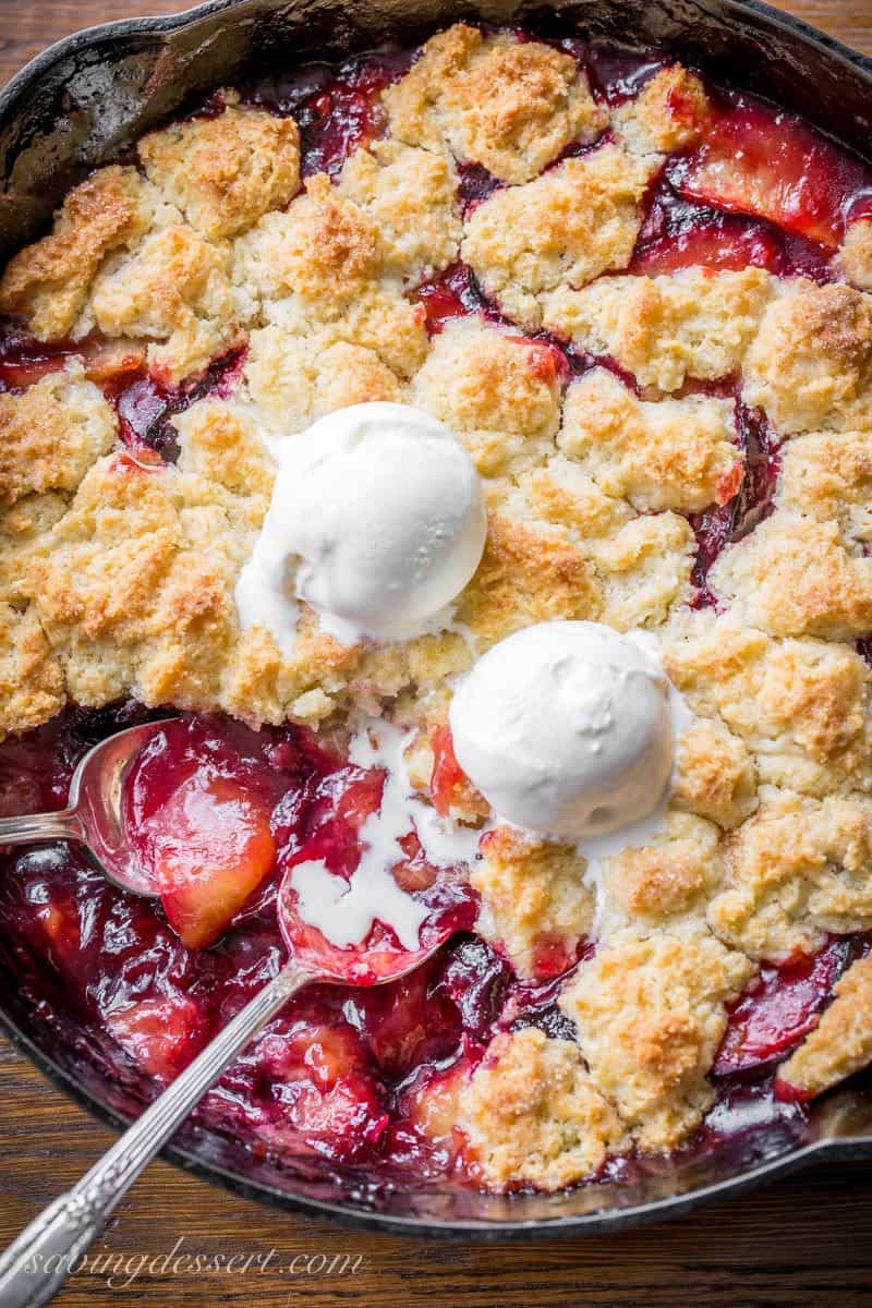 A cast iron skillet filled with a fruit dessert with a crumbled dough on top with scoops of ice cream