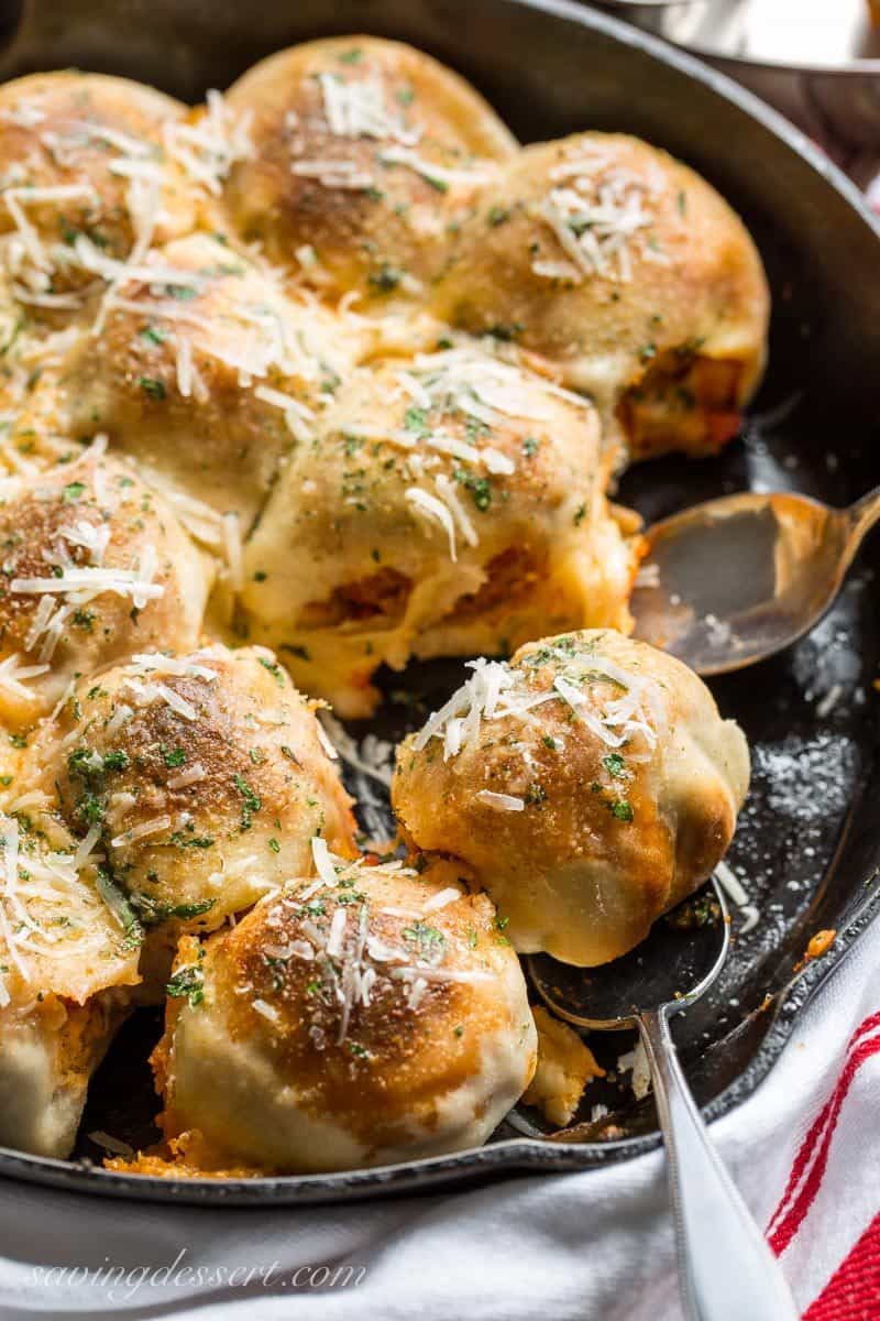 A cast iron skillet filled with pizza dough wrapped meatballs topped with Parmesan