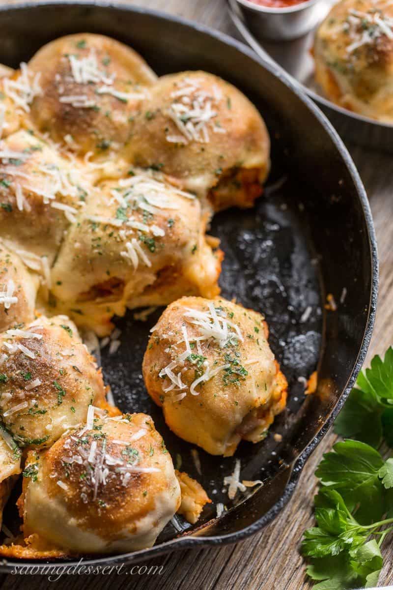 A skillet with meatballs wrapped in pizza dough sprinkled with cheese and garlic butter sauce