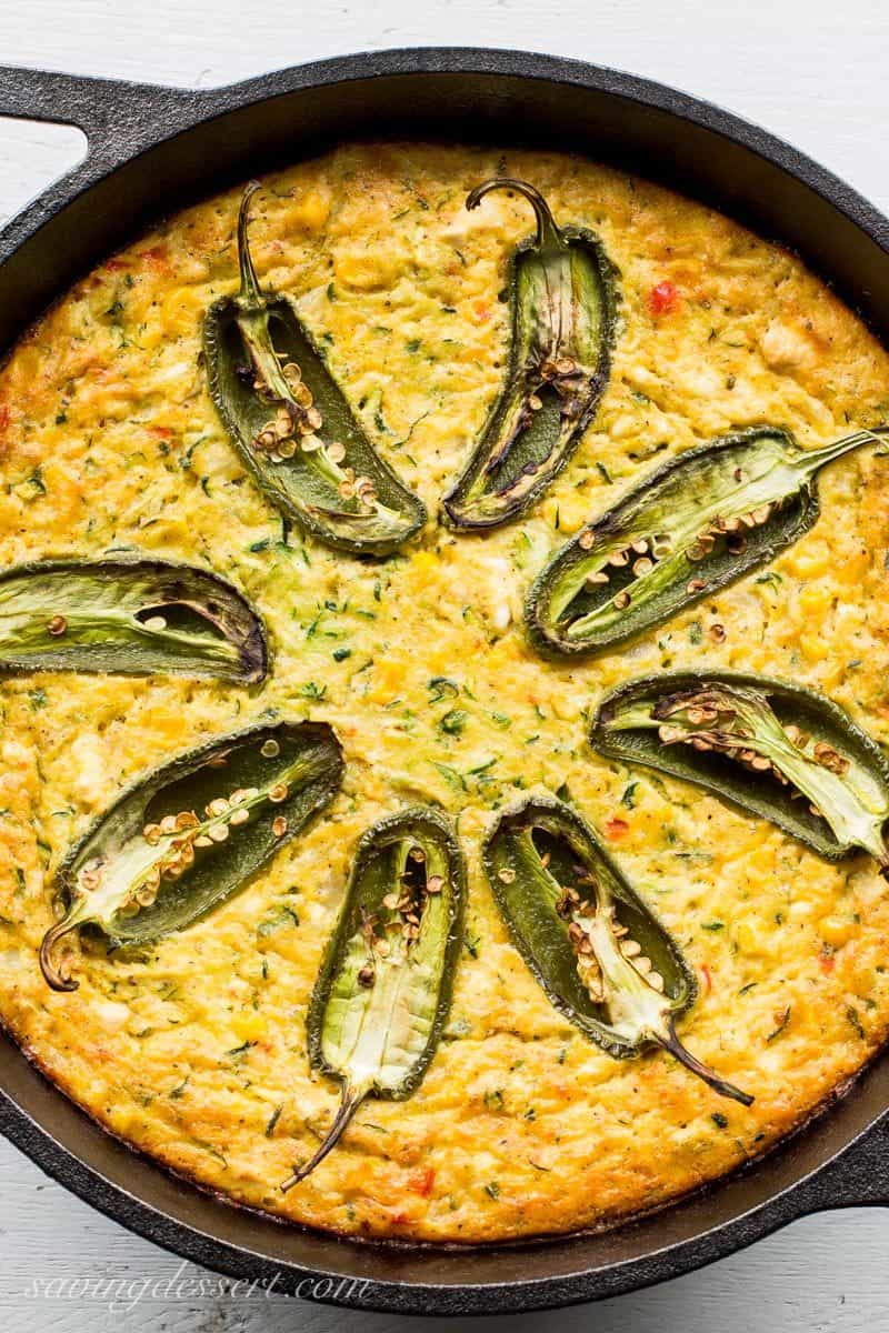 A corn and zucchini casserole in a cast iron deep dish skillet topped with jalapeño peppers