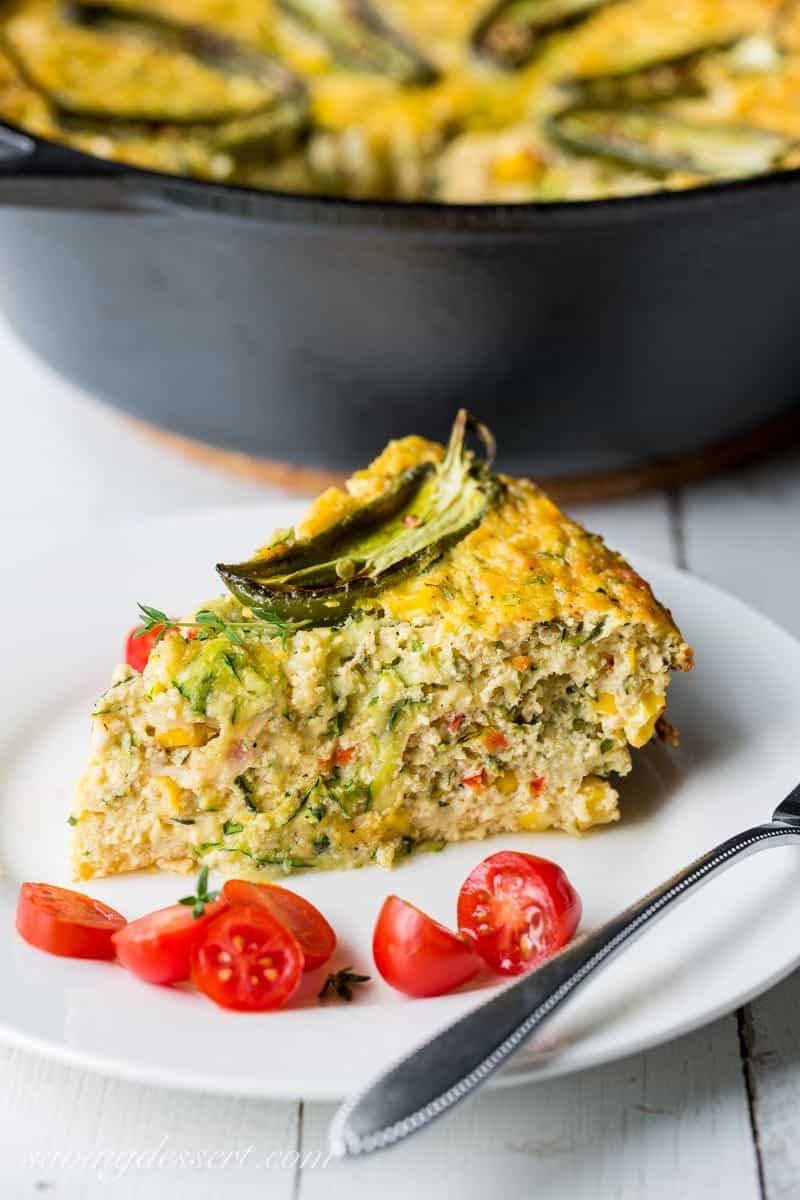 A slice of corn and zucchini casserole on a plate with tomatoes