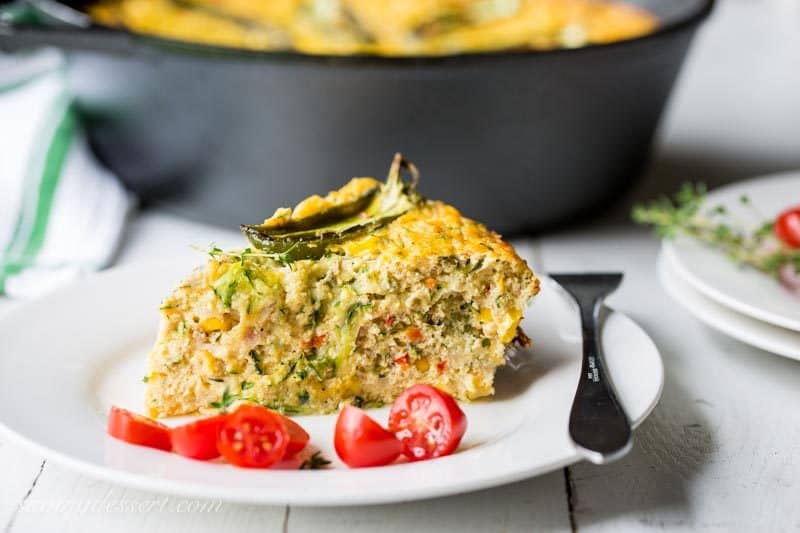 A slice of corn casserole on a plate with tomatoes