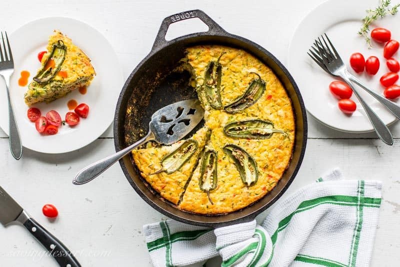 A sliced corn and zucchini casserole on a table served with tomatoes