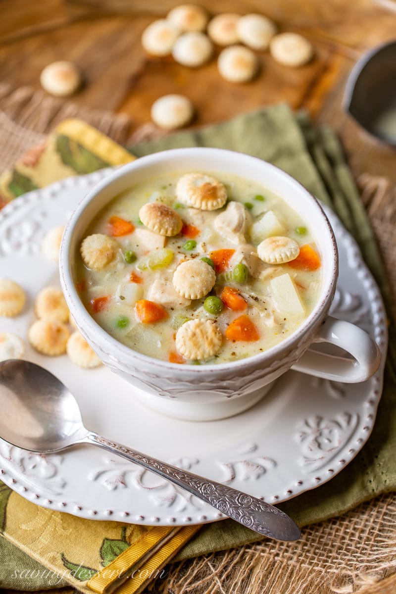 A cup of chicken pot pie soup with carrots, peas and oyster crackers