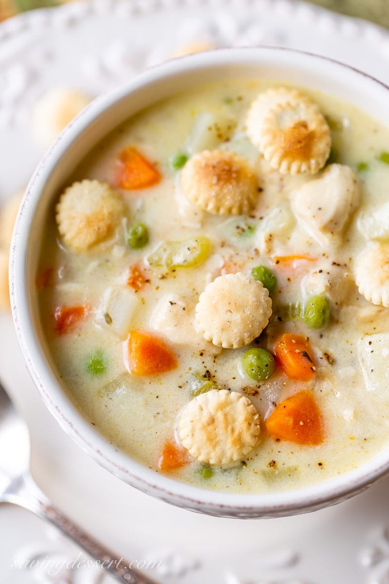 A bowl of chicken pot pie soup with carrots, peas, potatoes and oyster crackers on top