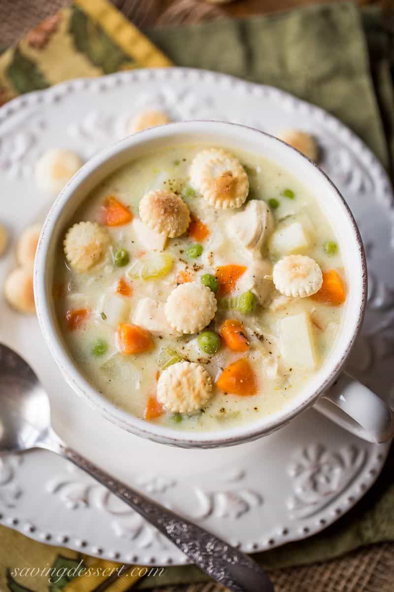 a bowl of creamy chicken pot pie soup with carrots, potatoes and peas and oyster crackers on top