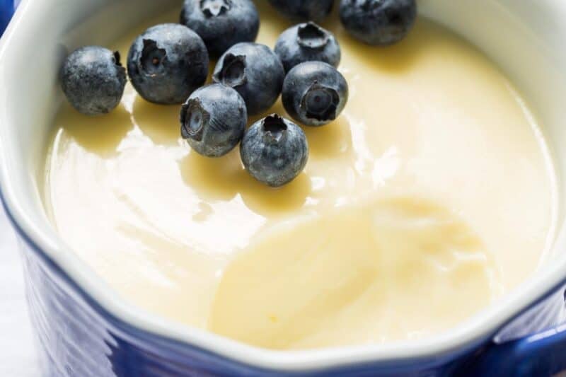 Overhead view of a small blue bowl filled with lemon posset with blueberries on top