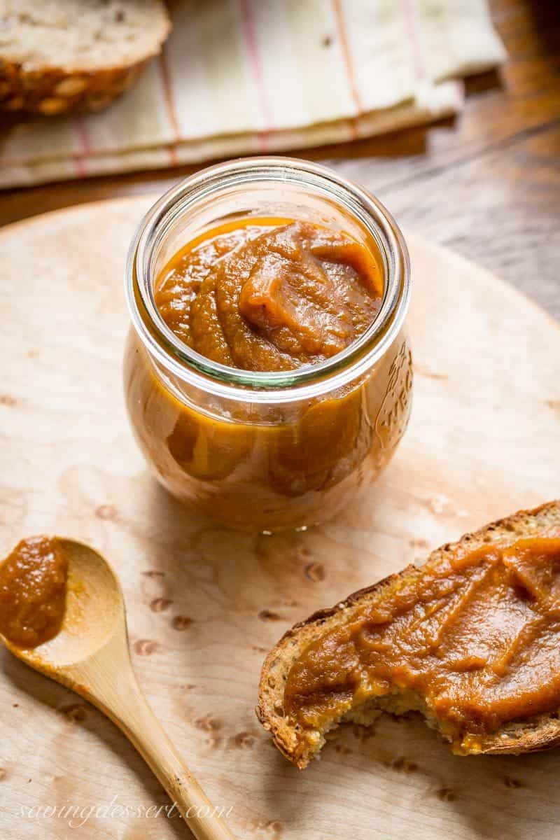 A jar of pumpkin butter on a cutting board with a spoon and slice of toast